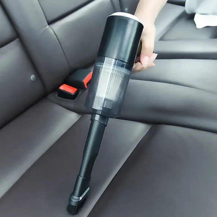 Hand holding a handheld vacuum cleaner inside a car.