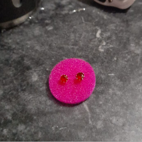 Pink earrings with red gemstones on a gray surface next to a digital scale and black container.