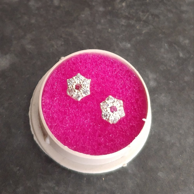Silver earrings on a pink cushion inside a round white container on a dark surface