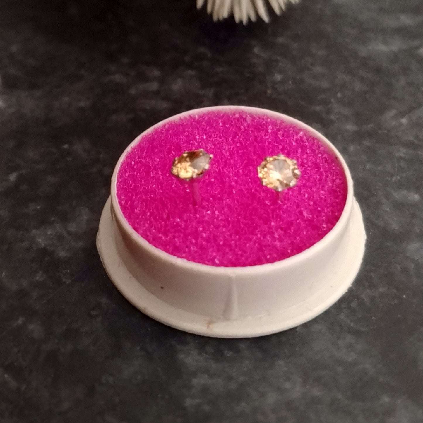 Pink earring box with earrings on a dark surface with flowers in the background