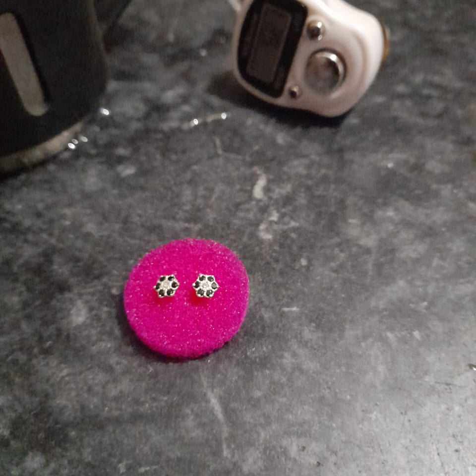 Pink earrings on a dark surface with a digital device and mug in the background