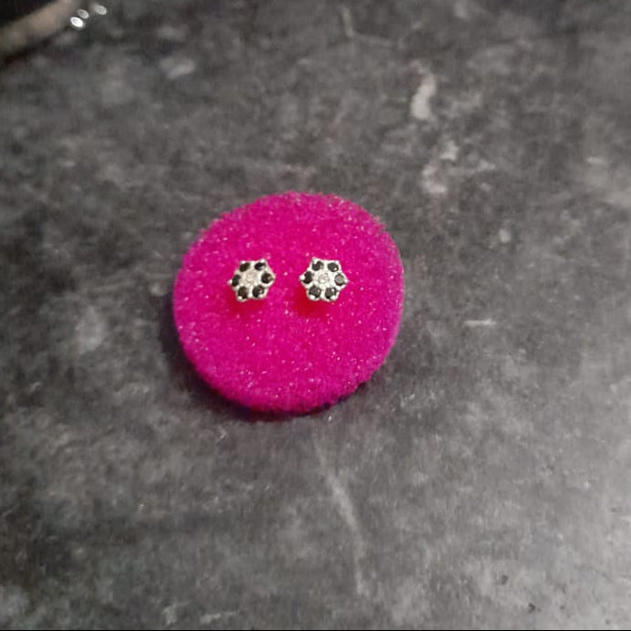 Pink earrings on a dark surface with a digital device and mug in the background