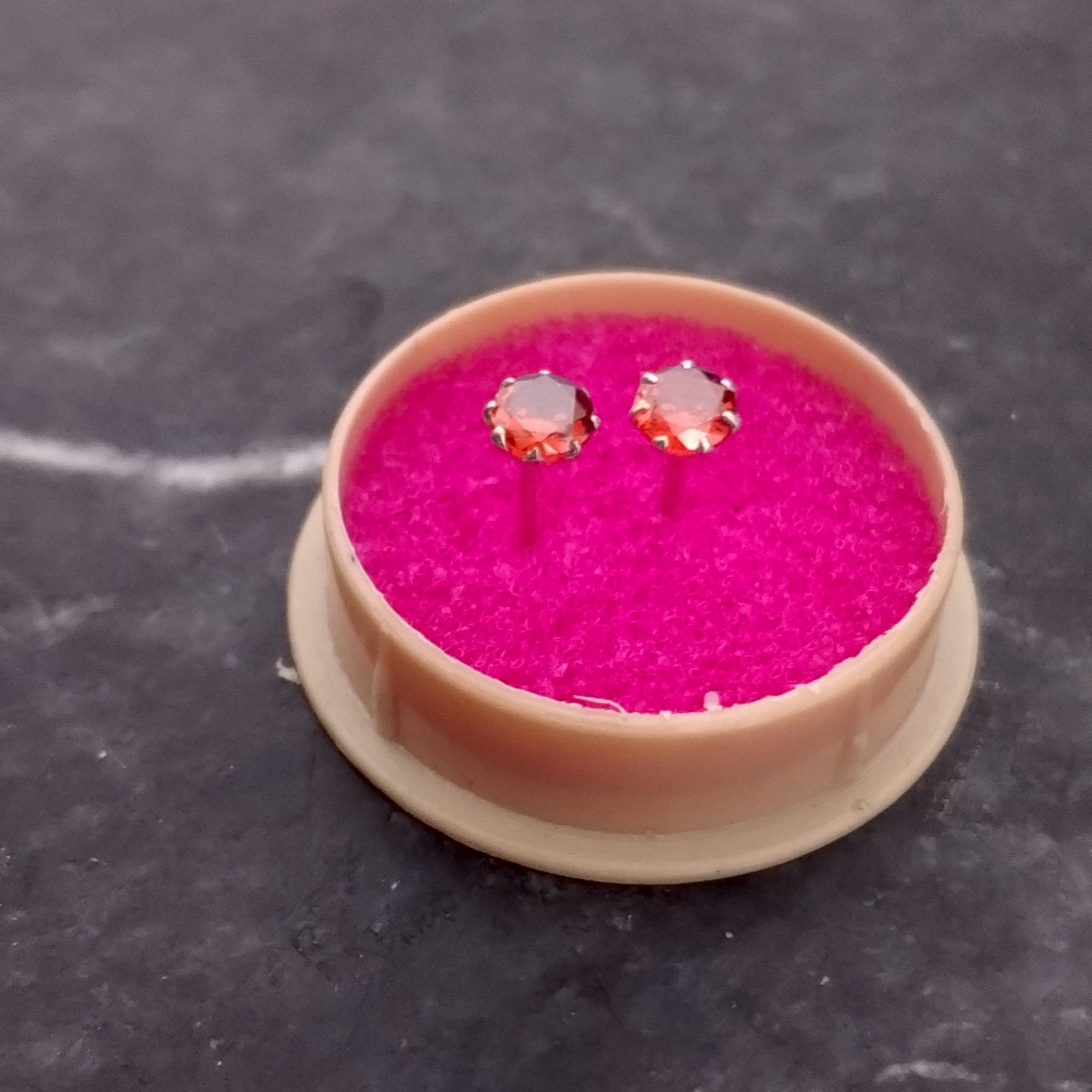 Small round container with pink fabric and gold earrings on a dark surface