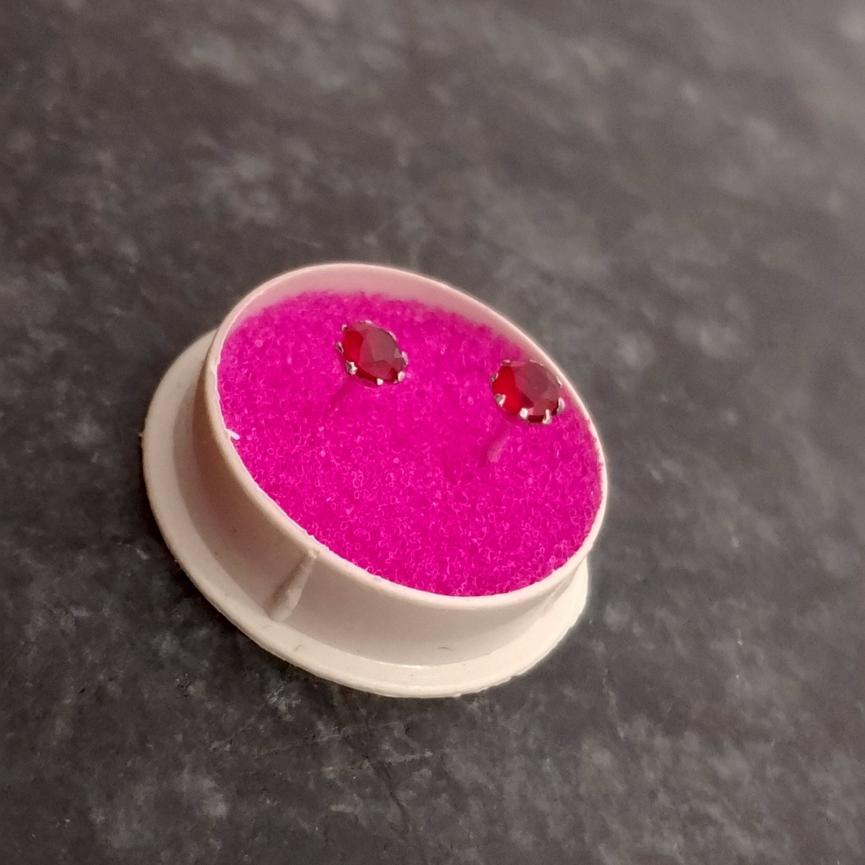 Pink earrings on a white stand with a dark background