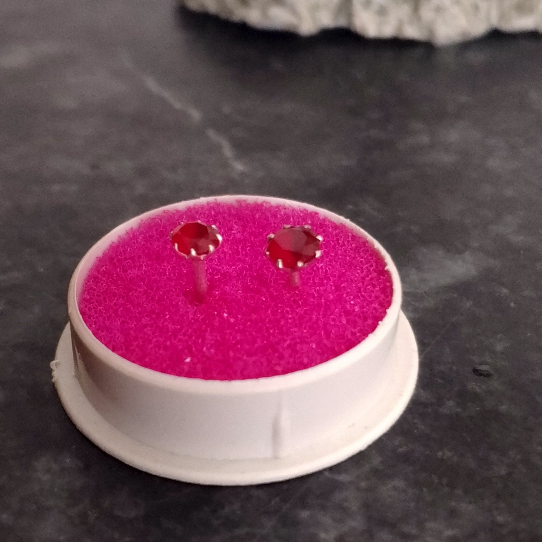 Pink earrings on a pink cushion with a gray rock and dark surface in the background