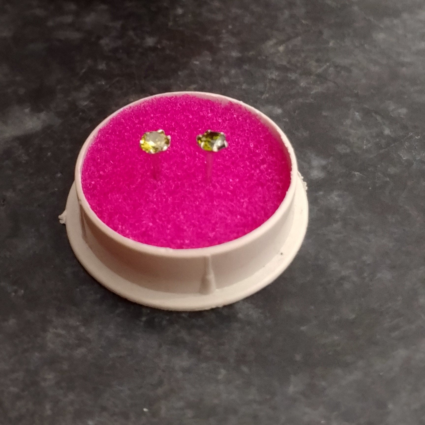 Round pink cushion with green gemstone earrings on a dark surface with flowers in the background