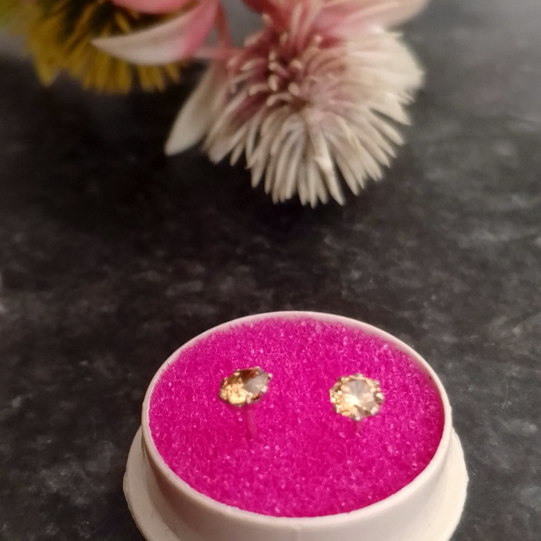 Pink earring box with earrings on a dark surface with flowers in the background