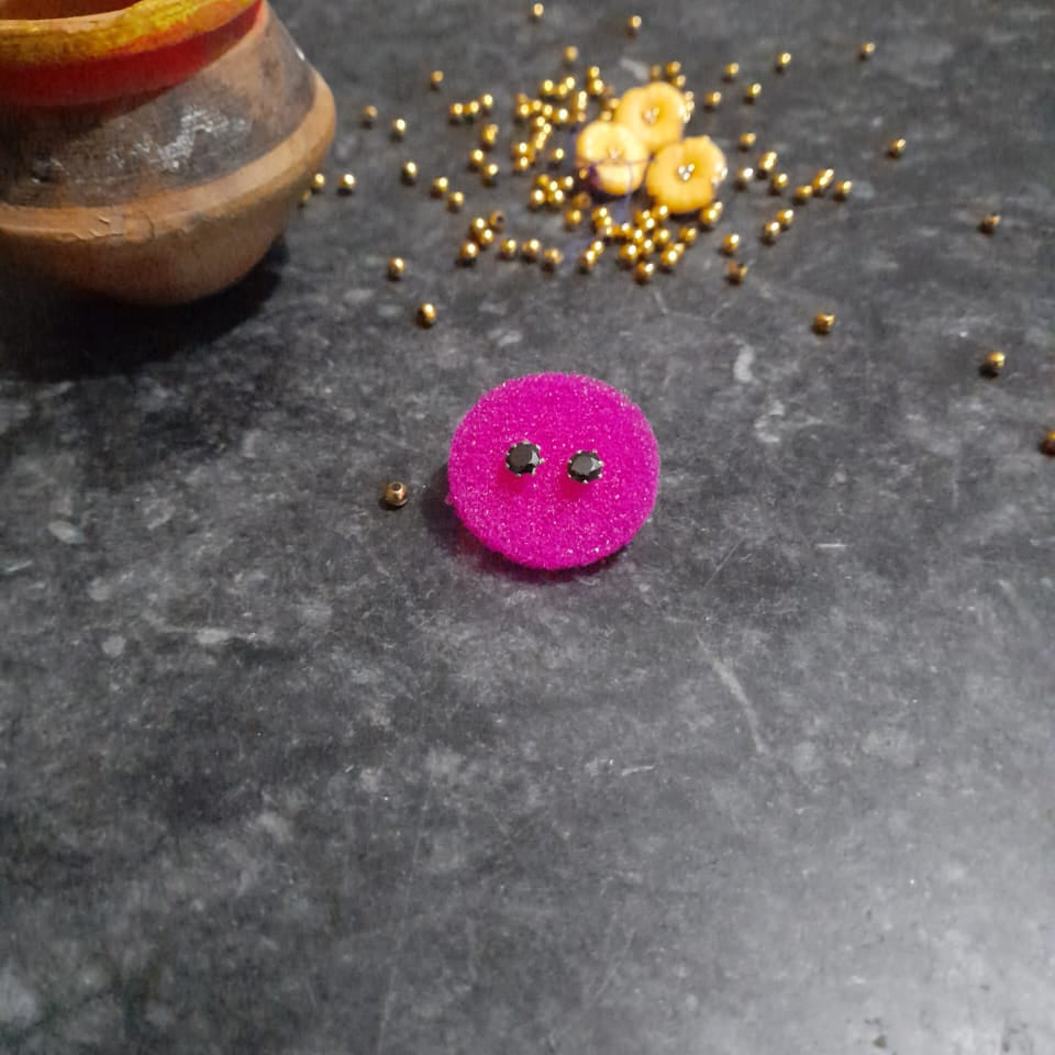 Purple circular object with black details on a dark surface with small yellow objects and a wooden container.